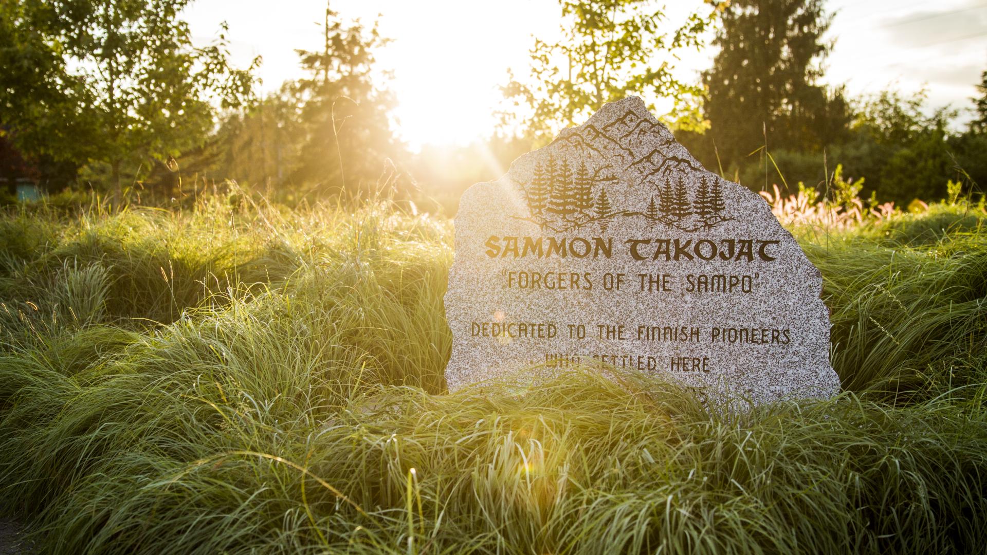 In a long grassy patch as the sun sets, a carved stone reads: "Sammon Takojat 'Foragers of the Sampo' Dedicated to the Finnish pioneers who settled here".
